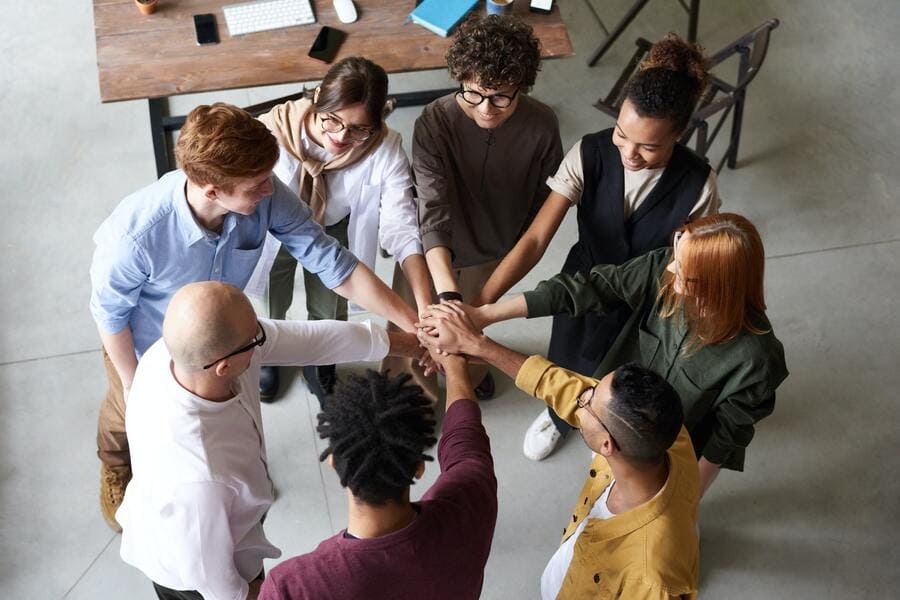 Male and female coworkers huddling put their hands in for a team spirit moment