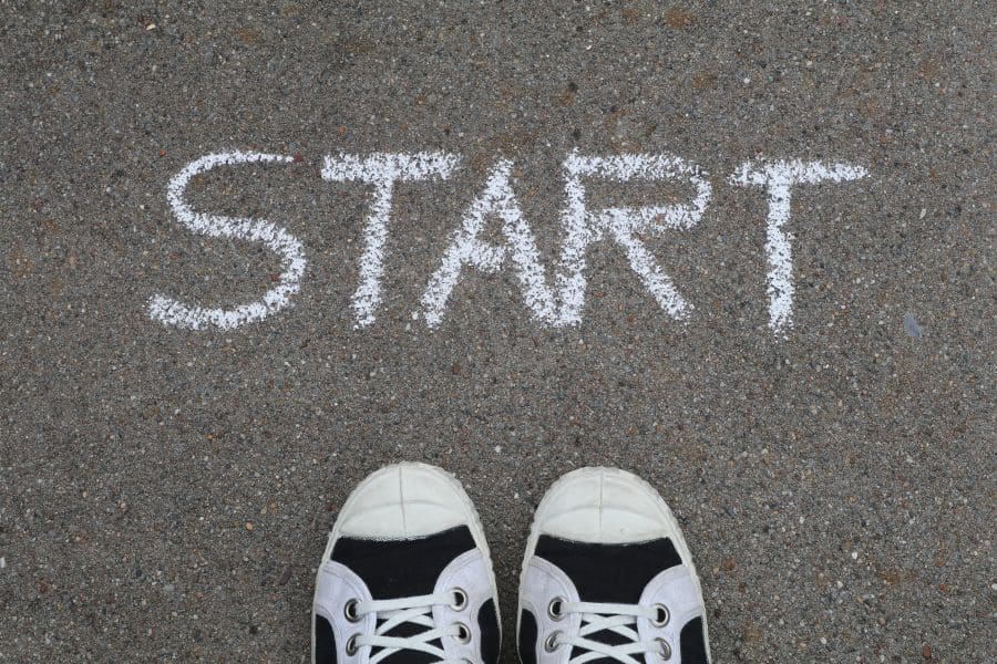sneaker tips pointing to the word "start" on asphalt