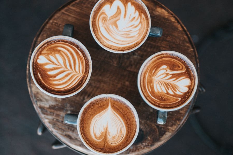four coffee cups from above with designs in the foam