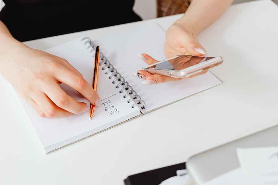a woman holding a phone writing in a notebook