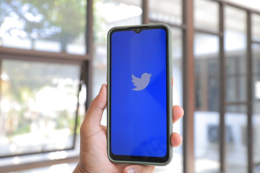 a hand holding a phone with the twitter logo on the screen