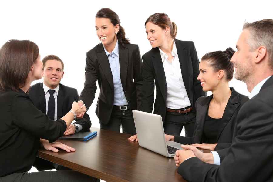 a group of adults in business dress shaking hands around a table