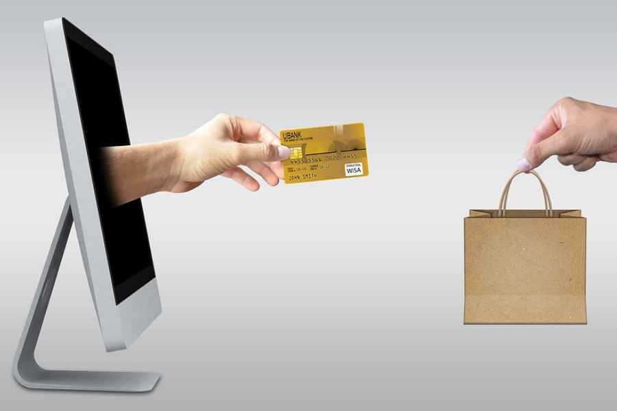 a hand with a credit card emerging from a computer screen and another hand holding a bag