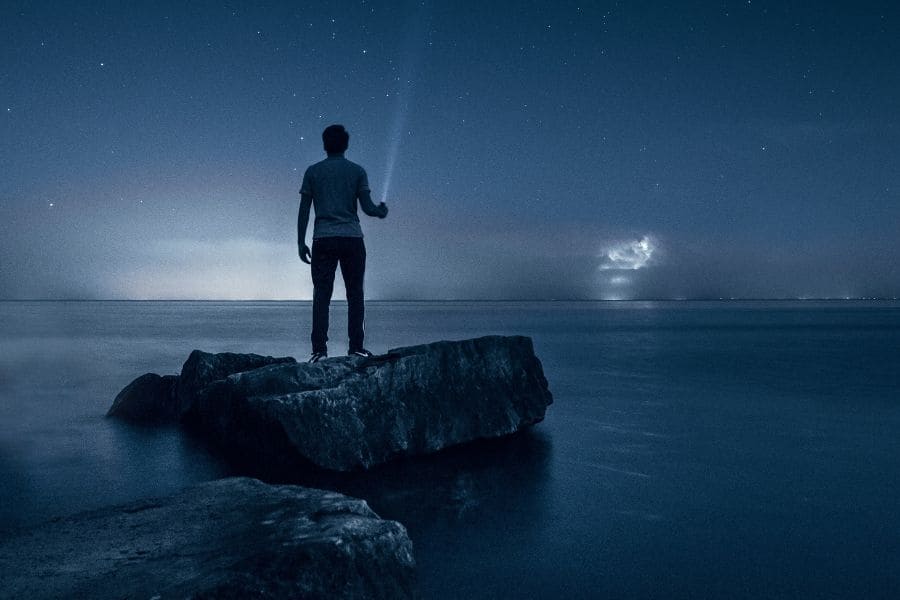 a man with a flashlight standing on a rock in the water