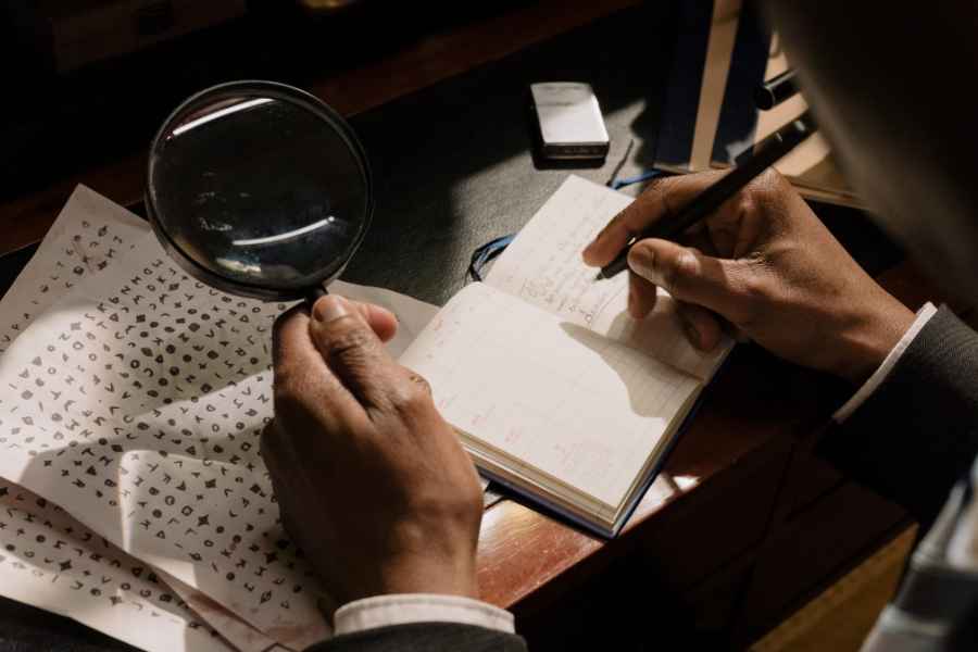 man with magnifying glass writes in notebook